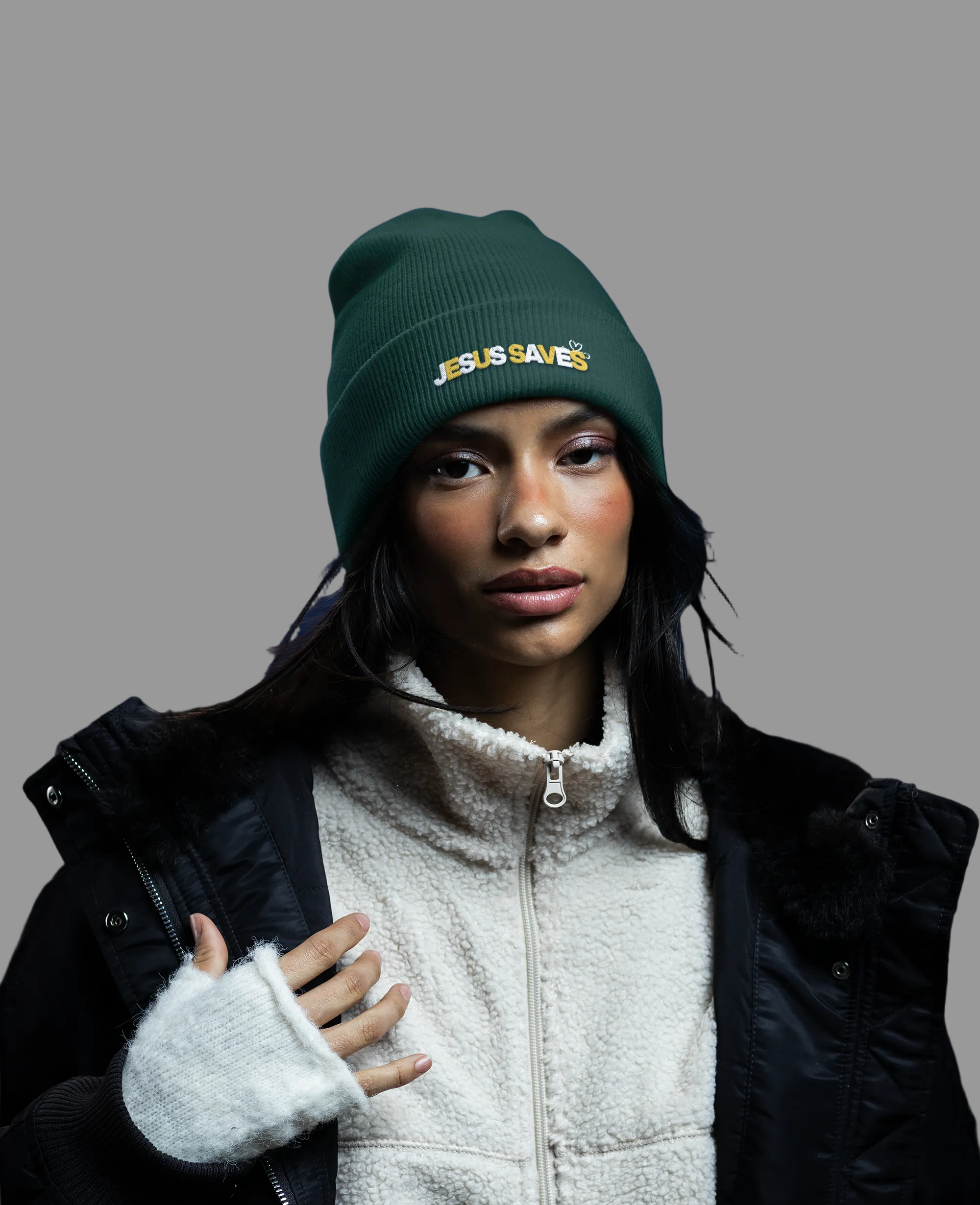 Person wearing a green beanie with 'Jesus Saves' text, black jacket, and white fleece-lined gloves against a dark blue background.